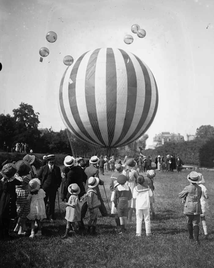 Children and adults gathered around a large striped hot air balloon in a magical historical photo colorized by viral artist.