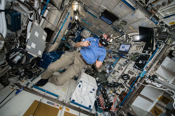 Astronaut wearing VR headset inside the space station, surrounded by equipment and floating objects in zero gravity.