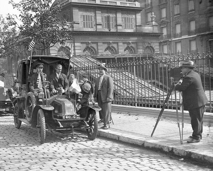 Early 1900s vintage car with American and French flags, photographed by a historical photos colorized artist on cobblestone street.
