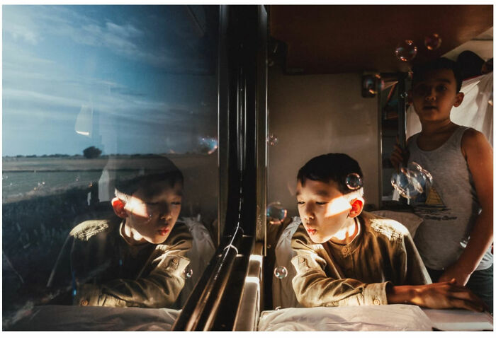 Young boy captured through the lens of a vagabond, blowing bubbles inside a train with natural light from the window.