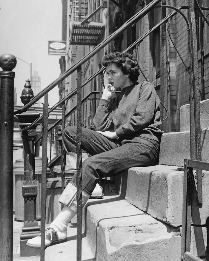 Colorized historical photo of a woman sitting thoughtfully on urban stone steps with vintage iron railings.