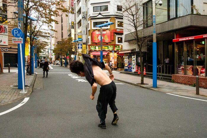 Street photographer capturing a spontaneous moment of a man bending backwards on a quiet urban street during the day.