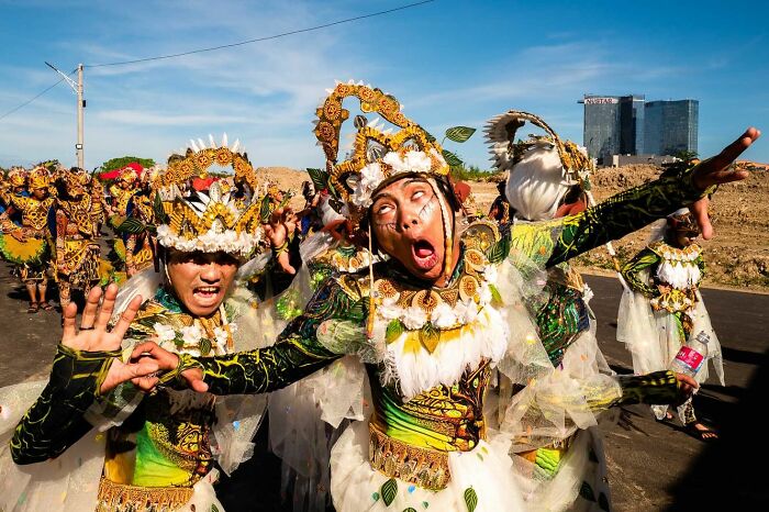 Street photographer captures vibrant dancers in traditional costumes making expressive faces during outdoor festival.