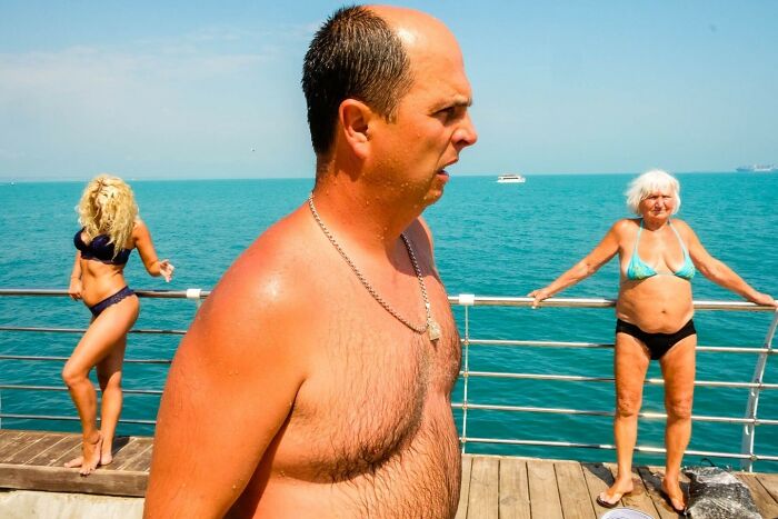 Man and two women in swimwear on a sunny pier by the sea, candid street photo capturing everyday moments.