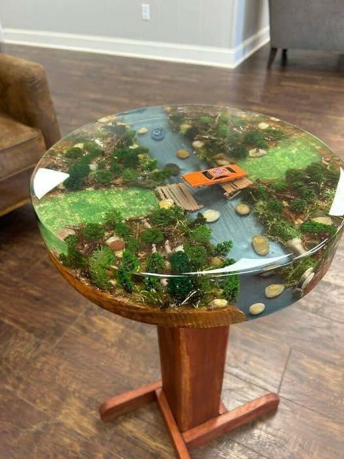 Crafted table with resin top featuring a miniature river scene and toy car, showcasing one of the horrible crafts shamed by netizens.