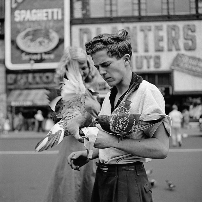 Young man in a yellow shirt feeding pigeons on a busy street, colorized historical photo by a talented viral artist.