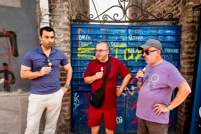 Three men enjoying ice cream in front of a graffiti-covered wall showing candid moments of street photography.
