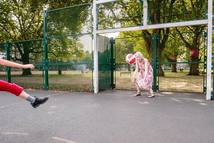 Elderly woman in a pink dress playing basketball outdoors, capturing a candid moment of street photography.
