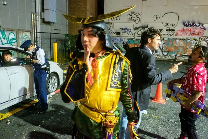 Street photographer captures a candid moment with a man in costume and others in a lively urban setting at night.