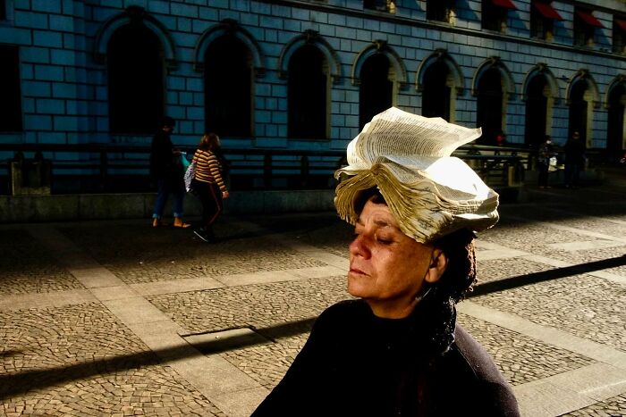 Woman with an open book on her head caught by street photographer on a sunny city sidewalk with shadows and pedestrians.