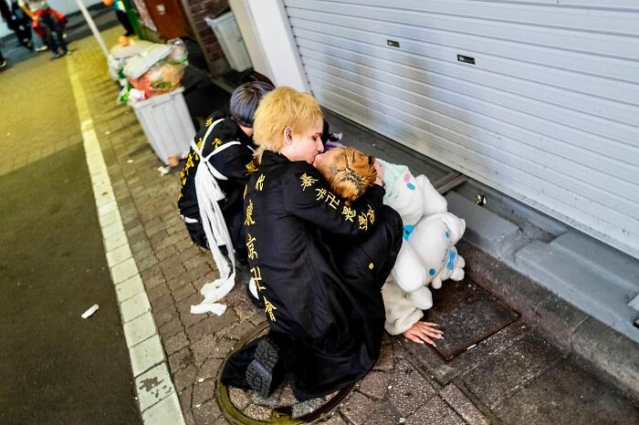 Street photographer captures candid moment of people in costumes embracing on a city sidewalk at night.