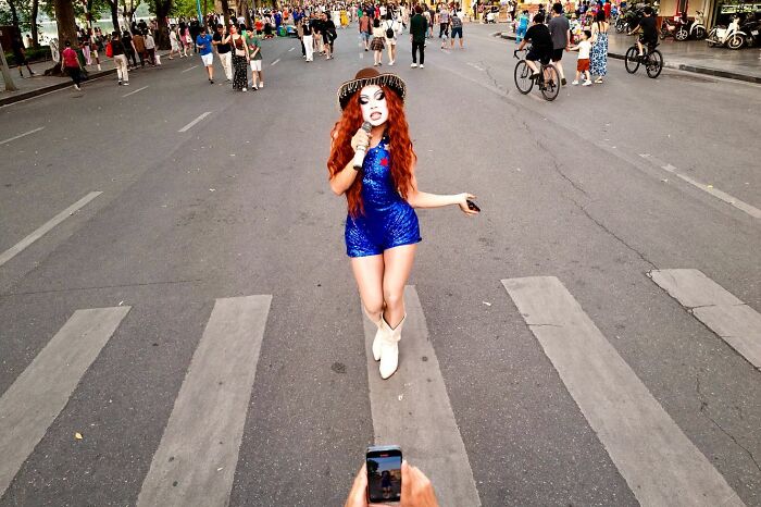 Candid street photo of a woman in a blue dress posing on a busy city crosswalk, captured by award-winning photographer.