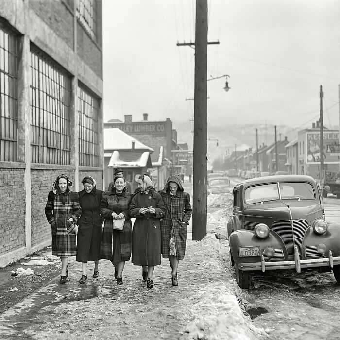 Five women in colorful vintage coats walking on a snowy street with a classic car, a magical historical photo colorized.