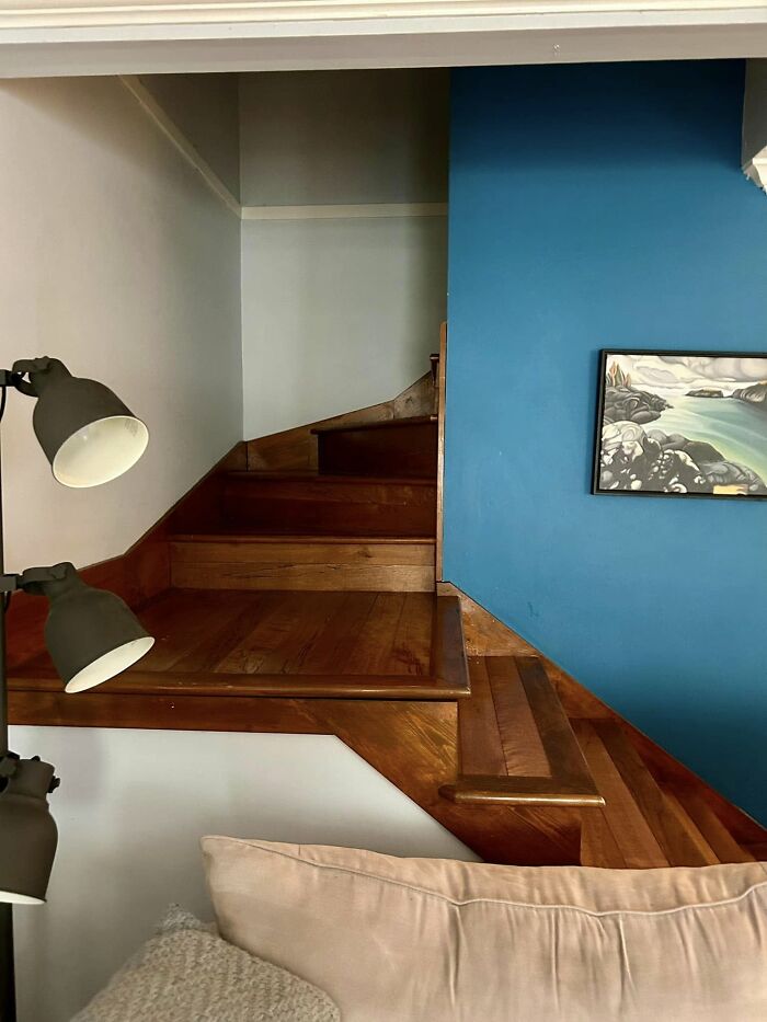 Wooden death stairs with sharp turns inside a home, next to a blue wall and a beige couch, posing a dangerous option.