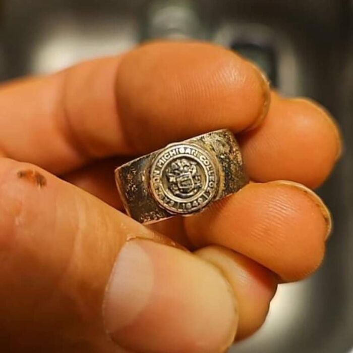Close-up of a hand holding an old college ring, one of the surprising things people found in walls or other places.