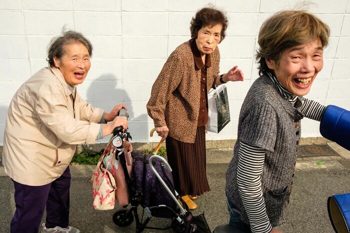 Three elderly women smiling and walking outdoors, captured by a street photographer catching the world off guard.