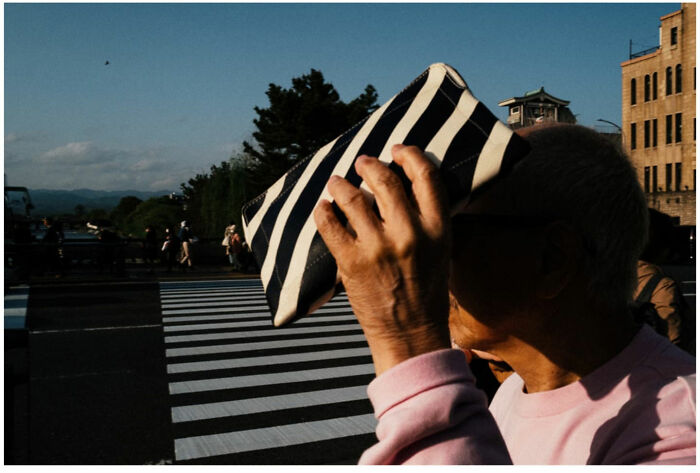 Elderly person shielding face with striped bag on busy street, capturing raw moments from the streets of Asia and beyond.