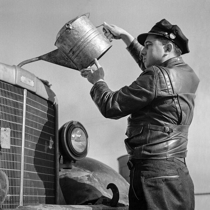 Man in leather jacket pouring oil into vintage car engine in a colorized historical photo by viral artist