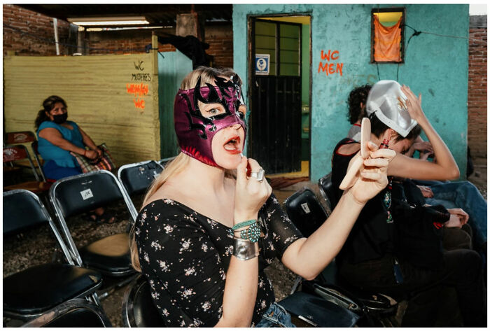 Woman wearing a colorful mask applying makeup in a lively street setting, capturing raw and captivating moments of Asia.