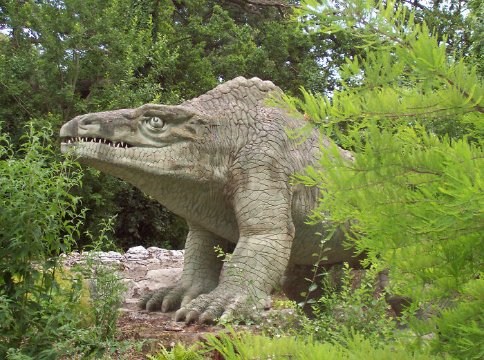 Life-like dinosaur model standing among lush green plants, showcasing fascinating dinosaur facts and realistic details.