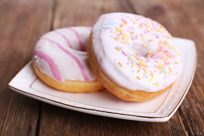 Two pink-frosted donuts with sprinkles on a white plate on a wooden table, representing a priceless reward after a dollar.