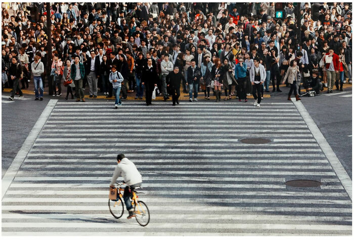Crowded Asian city street with pedestrians waiting to cross and a lone cyclist riding across a large crosswalk.
