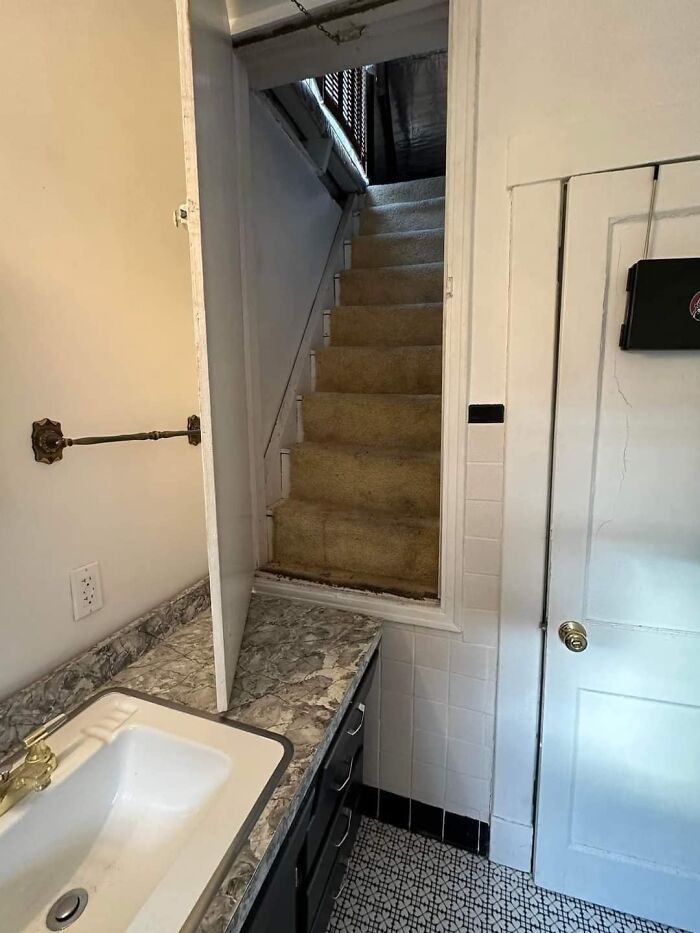 Narrow, steep death stairs with carpet leading from a small bathroom with tiled floor and marble countertop