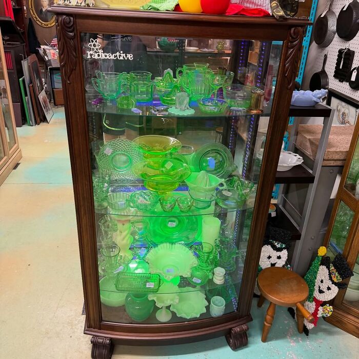 Glass display cabinet filled with cool secondhand finds including vintage green glassware and collectible items in a thrift store.