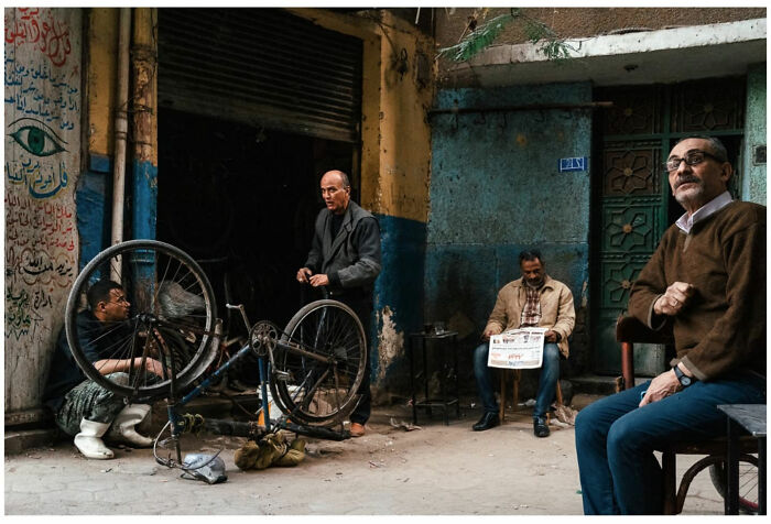 Four men in a rustic Asian street setting, one fixing a bicycle, capturing raw and captivating moments of daily life.