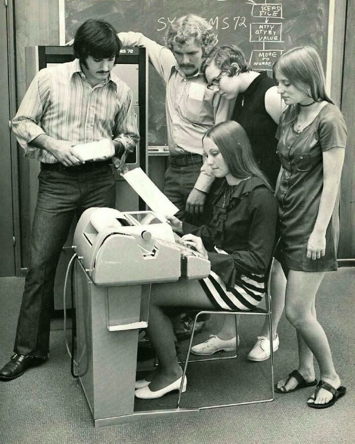 Group of young adults using an early computer terminal in a vintage setting, colorized by a talented viral artist.