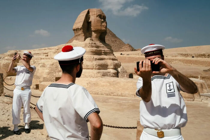 Three sailors in uniform taking photos at the Great Sphinx, capturing raw and captivating moments through the lens of a vagabond.