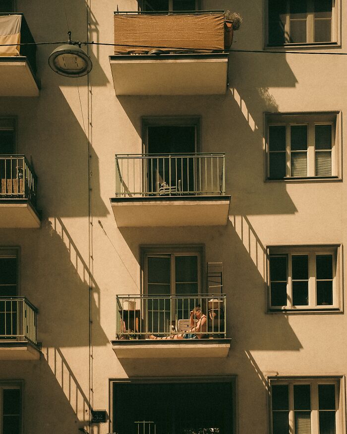 Urban photo of a person relaxing on a balcony in Helsinki, capturing real street moments with cinematic lighting and shadows.