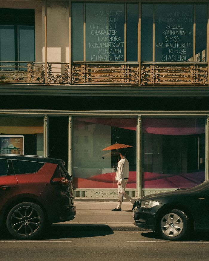Urban photo of a person with an umbrella walking between parked cars on a city street, captured like a real movie still.