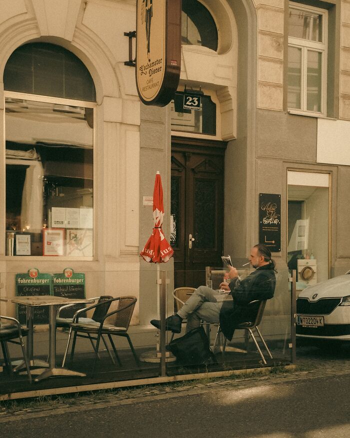 Man sitting at an outdoor café in an urban street scene, captured by a Helsinki-based photographer.
