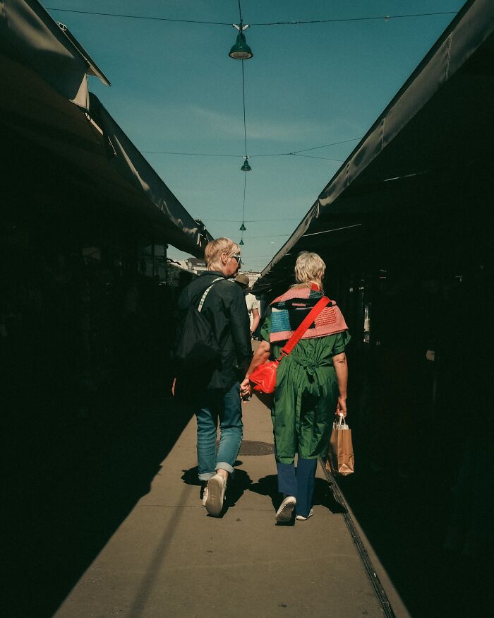 Urban street photo by Helsinki-based photographer showing two people walking between market stalls in natural light.