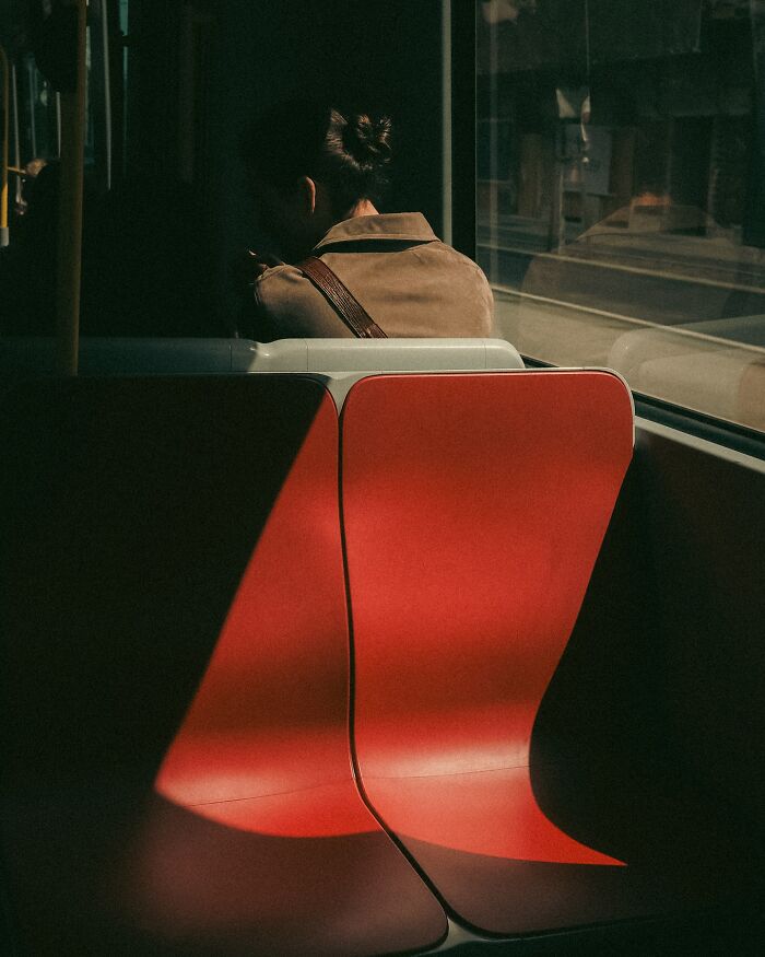 Woman sitting alone on red bus seats in an urban scene, a real moment captured by Helsinki-based street photographer.