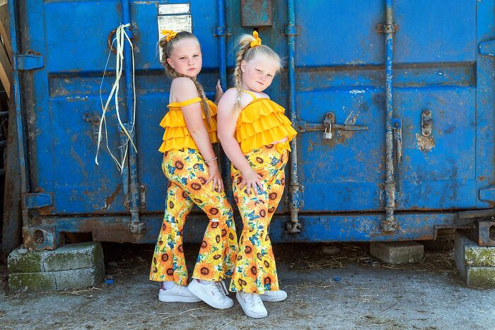 Two young girls in vibrant yellow outfits pose confidently against a weathered blue container, capturing life on the margins of modern Ireland.