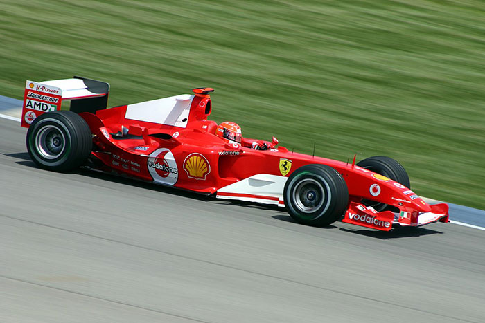 Red Formula 1 Ferrari car driven by Michael Schumacher speeding on a racetrack during a competitive race event.