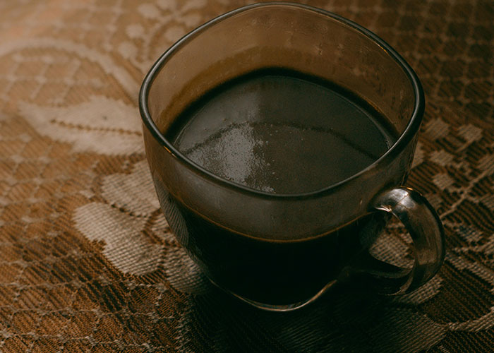 Close-up of a clear glass cup filled with dark coffee on a patterned brown tablecloth, illustrating take one for the team moments.