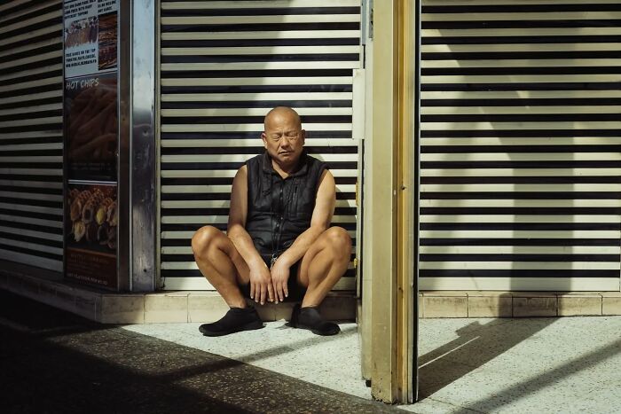 Man sitting on the floor in sunlight and shadows, captured in a candid street photo by Alex McClintock.
