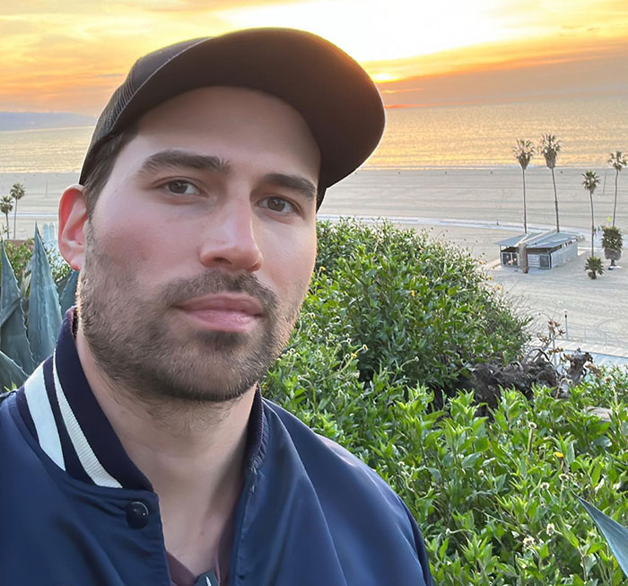 Man wearing a black cap and jacket with a sunset beach background, related to Tyler Perry harassment messages.