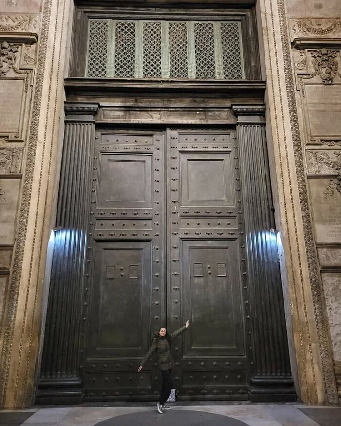 Person standing by an enormous ancient metal door surrounded by detailed stone carvings in archaeology world historical site.