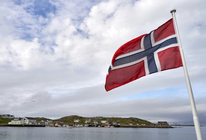Norwegian flag waving by a coastal village, showcasing one of the best countries to live in 2025 with scenic landscapes.