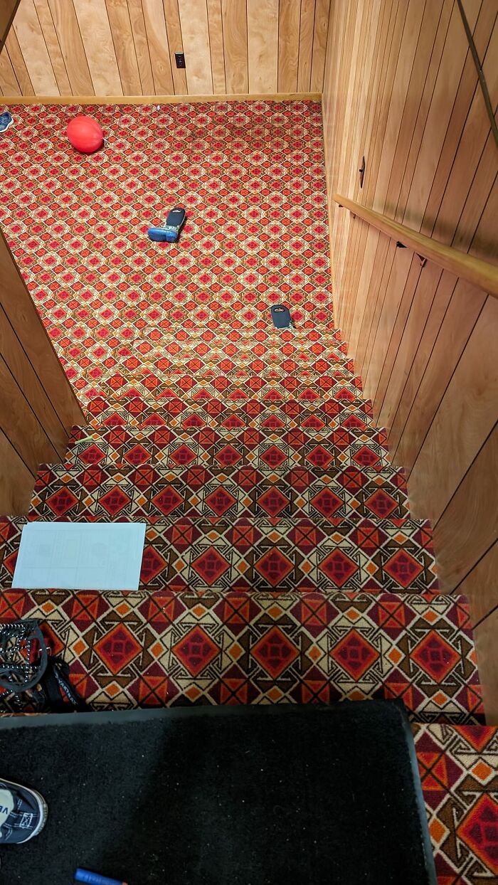 Steep death stairs covered in red patterned carpet with scattered toys and wood-paneled walls on both sides.