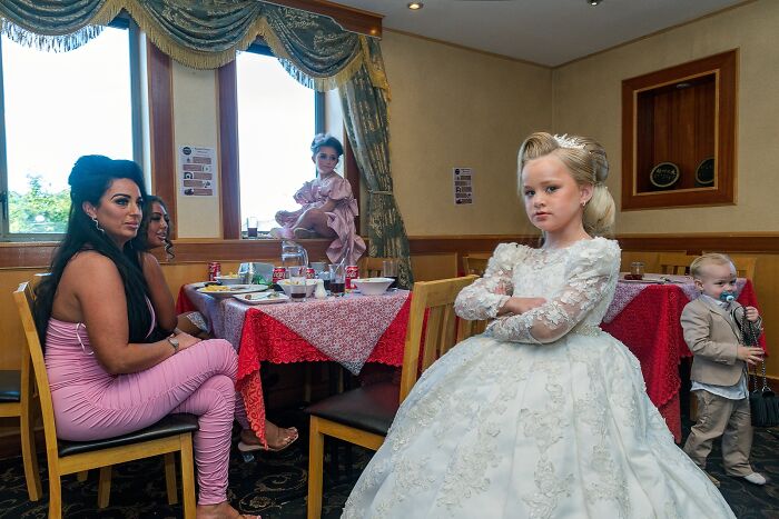 Young girl in a white dress and styled hair at a kitchen table, capturing life on the margins of modern Ireland.
