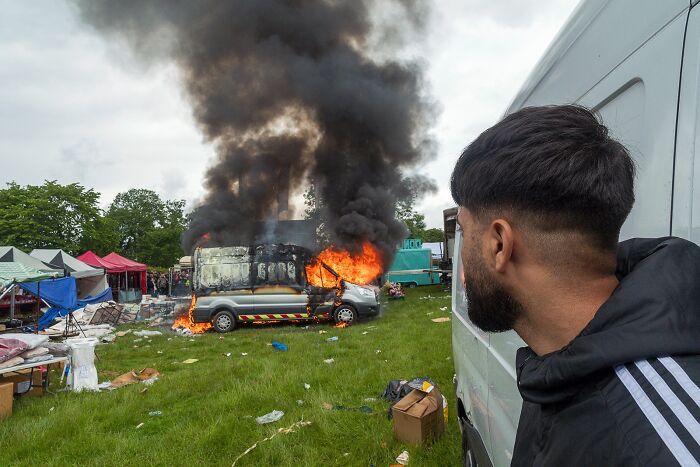 Man watching a van engulfed in flames and thick smoke in a grassy area, illustrating life on the margins of modern Ireland