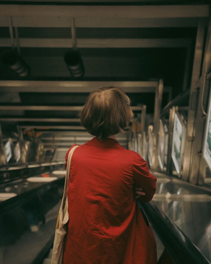 Person in a red coat riding an escalator in an urban setting captured by a Helsinki-based photographer street photo.