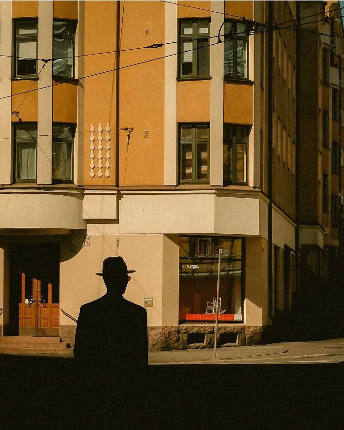 Silhouette of a man in a hat on a street corner in Helsinki, captured by an urban photographer in a cinematic style.