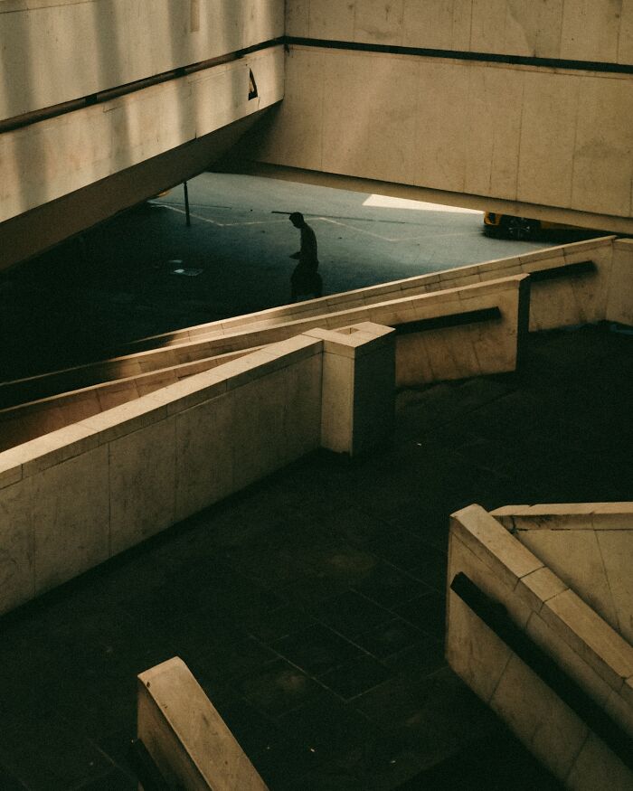 Urban photo showing a solitary figure in shadow amid concrete ramps and walls, capturing real moments caught on the street.
