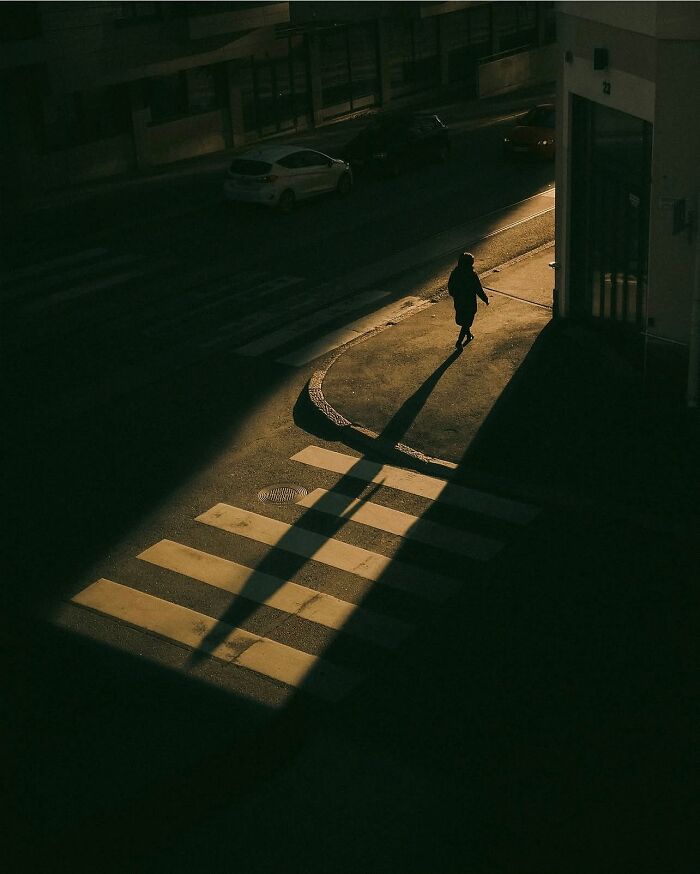 Person casting a long shadow while crossing a street in an urban scene captured by a Helsinki-based photographer.